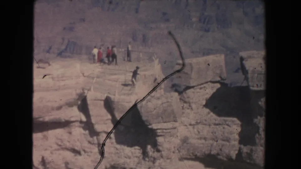 1951 home-movie frame showing distant tourists on a canyon overlook above shadowed rock ledges.