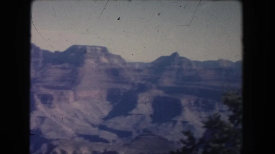 Soft 1951 8mm frame looking over New Mexico canyon formations, dark ravines, and a blurred tree or shrub at the lower right.