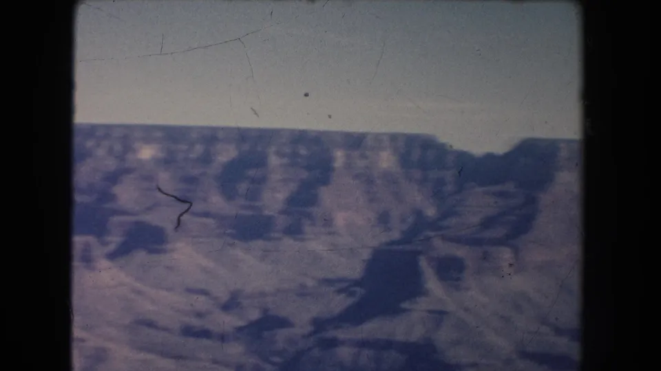 1951 New Mexico 8mm view of a broad layered canyon wall with dark rock shadows, pale sky, and visible film scratches.