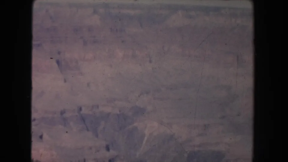 Faded 8mm frame of canyon formations, with the overlook figures no longer visible and terrain filling the view.