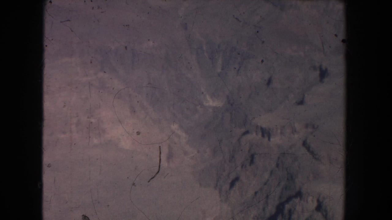 Muted dry valley terrain with pale slopes and dark rocky ridges.