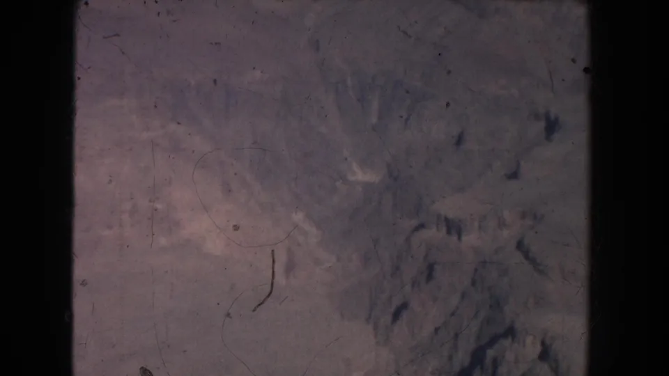 1951 New Mexico 8mm frame showing arid valley terrain, pale hillsides, and darker rock formations under a faded film scan.