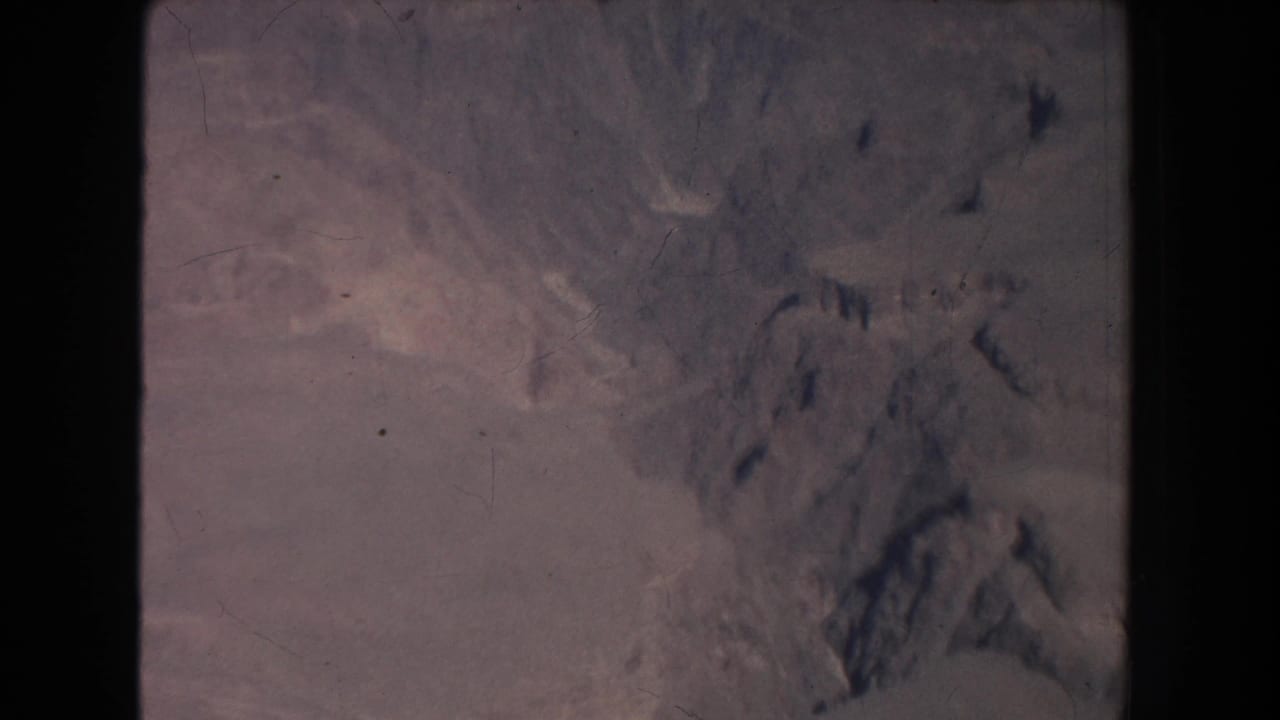 Arid hills and shadowed rock formations seen through a faded film frame.