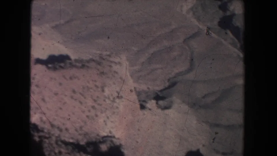 1951 New Mexico 8mm landscape frame with pale desert slopes, dark rock forms, and open arid terrain in a faded home-movie scan.