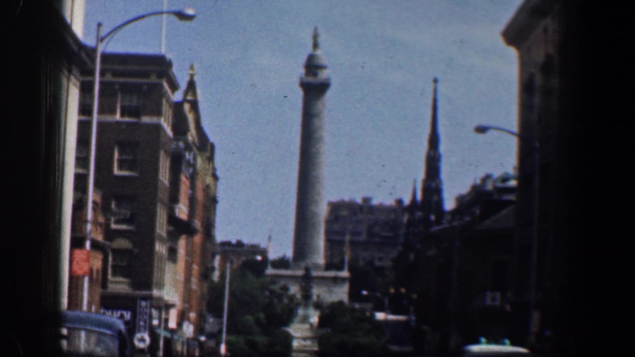 Tall monument and pointed spire above city buildings, with streetlights and a partial car below.
