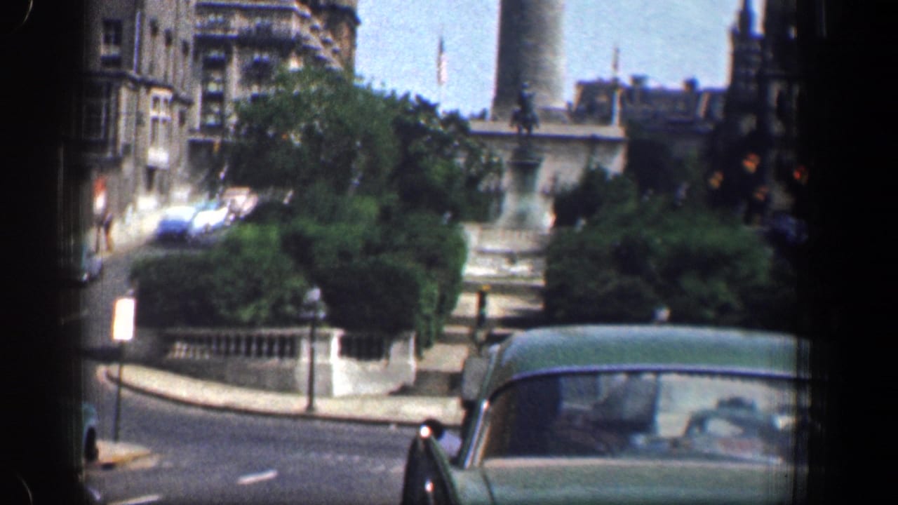 Washington DC street view from 1961 showing a green car, a stone civic setting, leafy trees, and a Gothic spire rising behind nearby buildings.