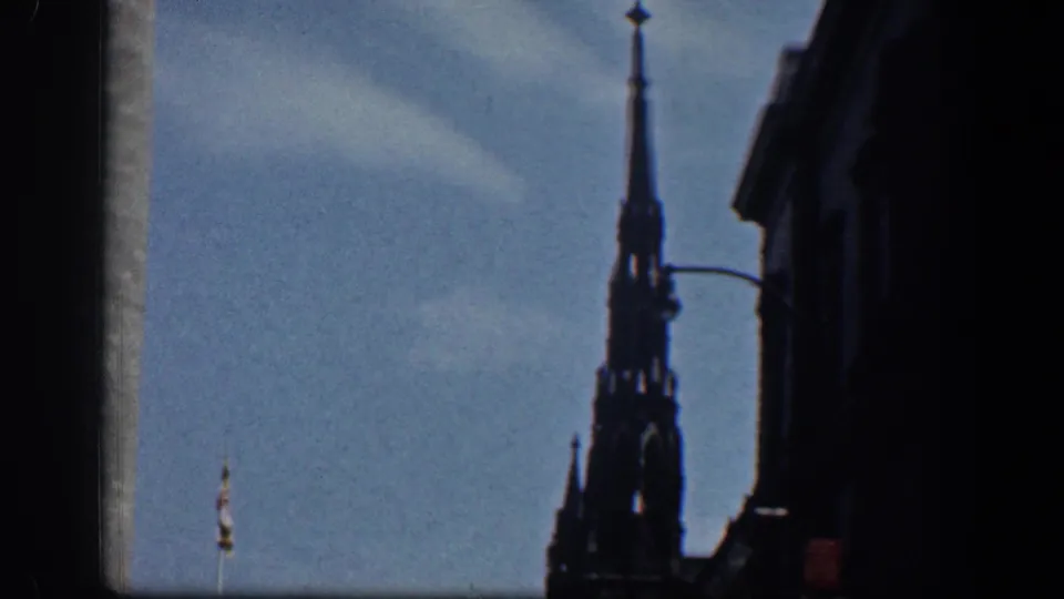 1961 Washington, DC home-movie frame showing a dark Gothic-style spire and nearby building edge against a blue sky.