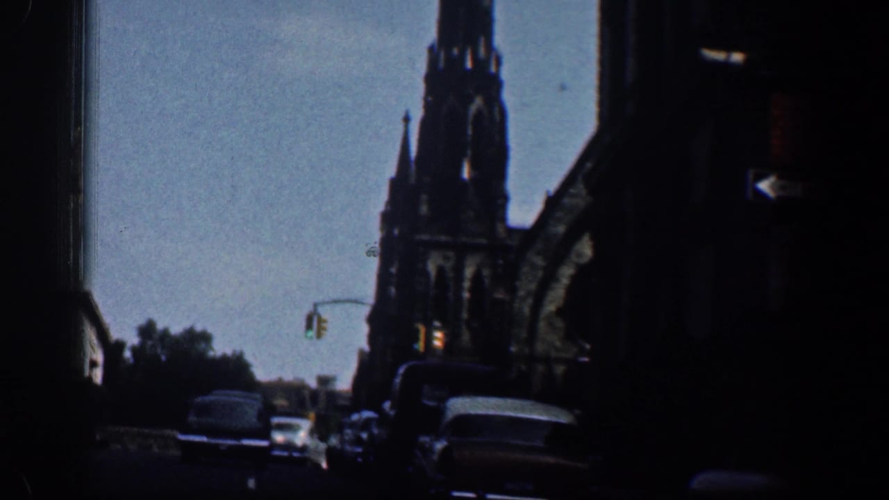 1961 Washington, DC home-movie view of a Gothic-style spire above a street with cars, trees, and a traffic signal.