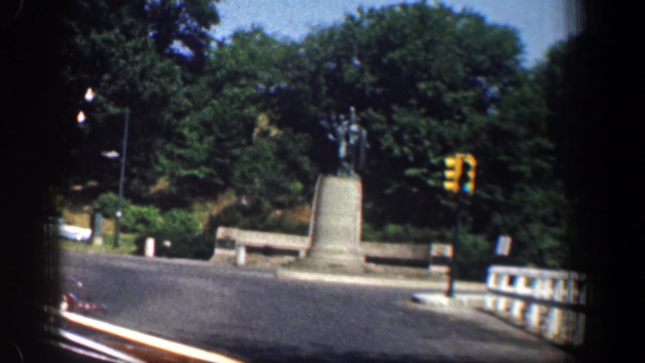 1961 Washington, DC home-movie view of a monument, traffic signal, bridge-like railing, and trees from a passing vehicle.