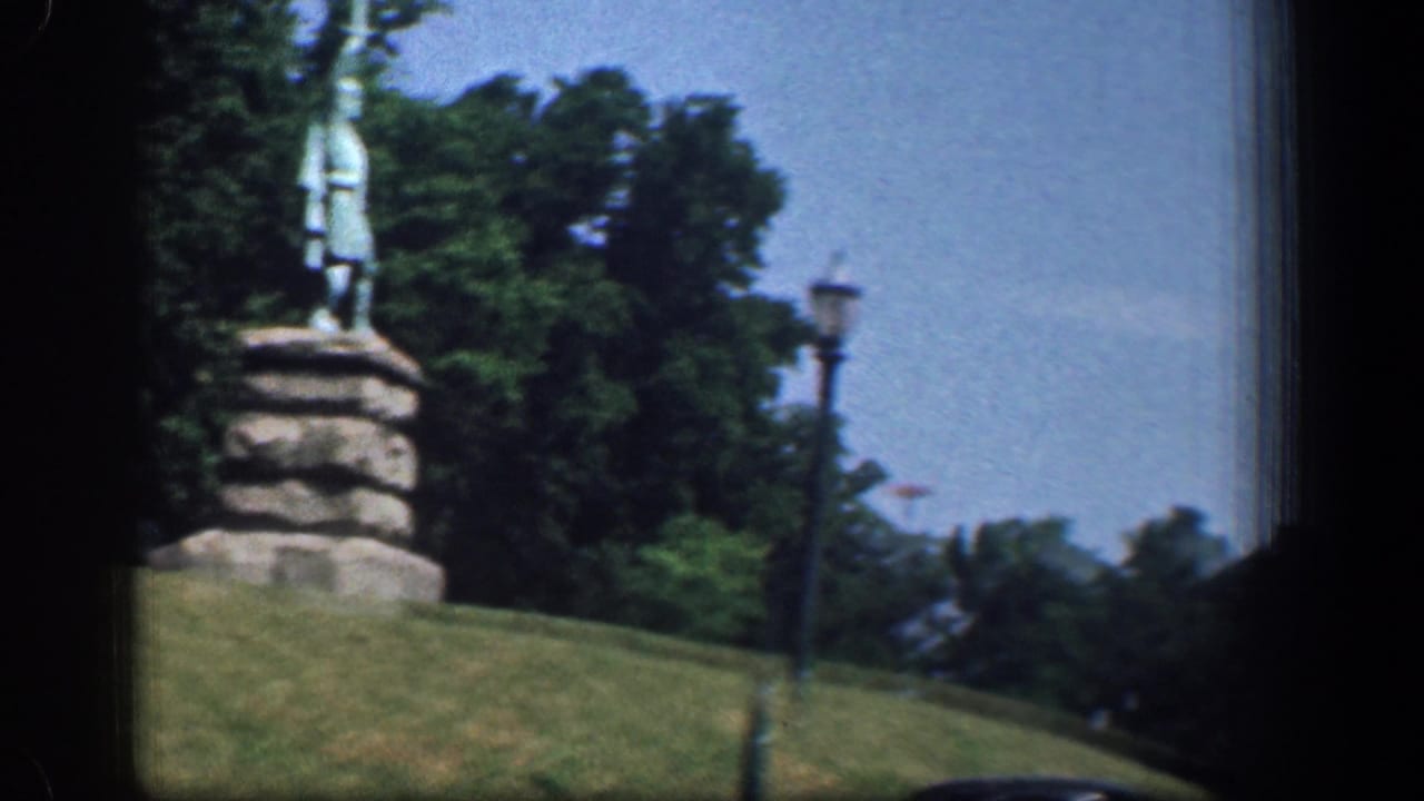 1961 Washington DC frame with the statue still near the center, set above a grassy slope with trees, sky, and a lamppost visible.