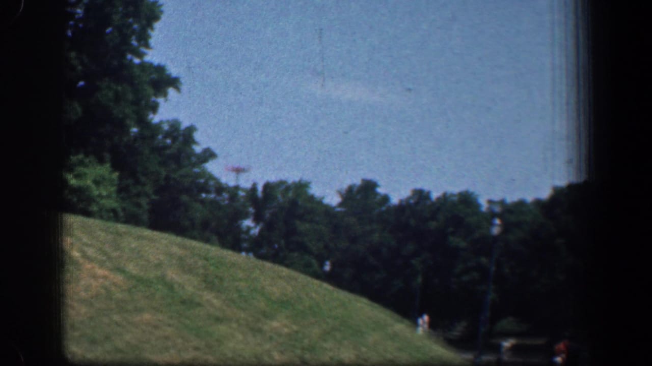 1961 Washington DC home-movie view of a green slope, tree line, roadside lamp, and a small distant pedestrian as the car passes the monument area.
