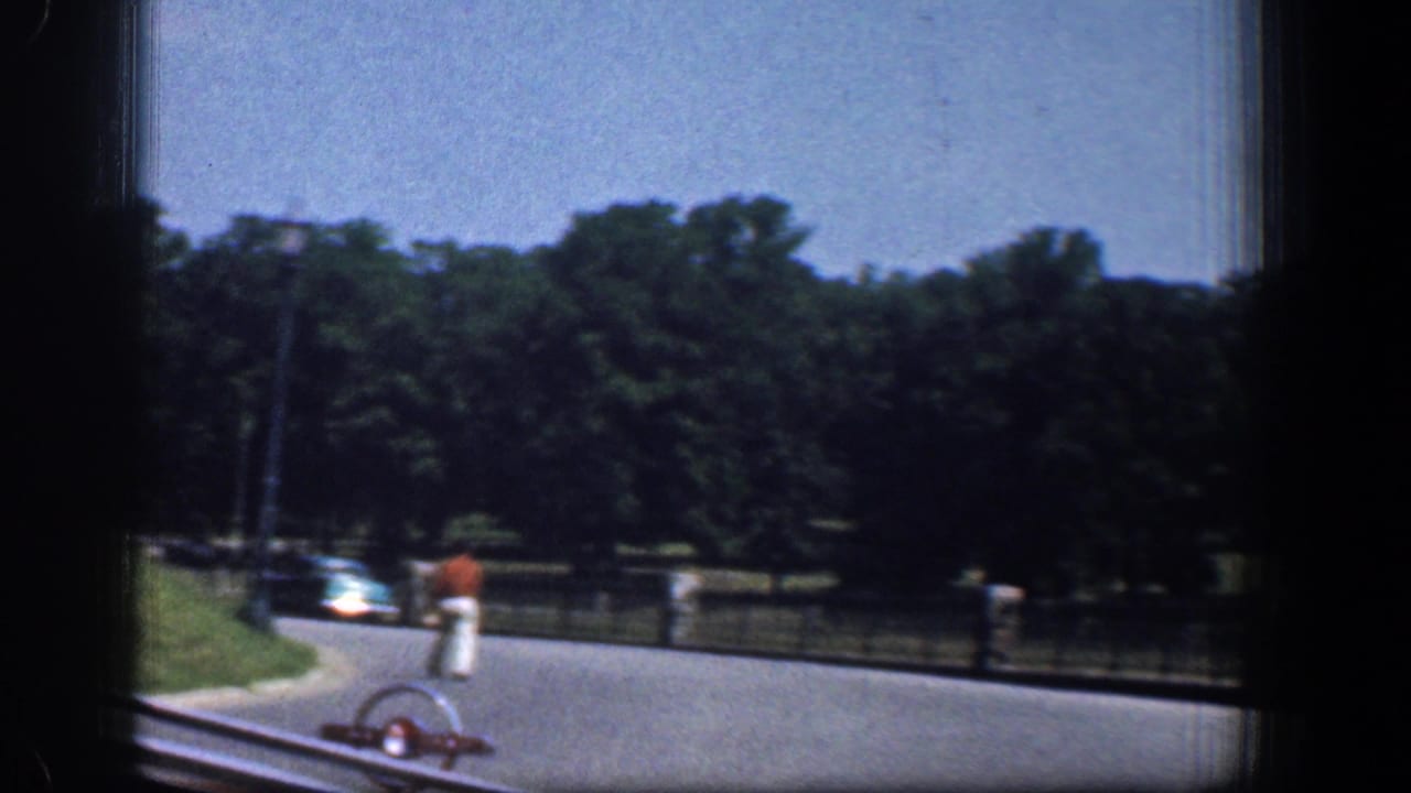 Paved park road seen through a car window with a walker in red and a distant light-colored car.