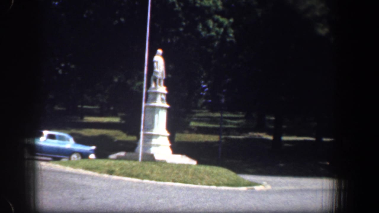 Roadside white stone statue on a grassy median with a blue sedan at left.