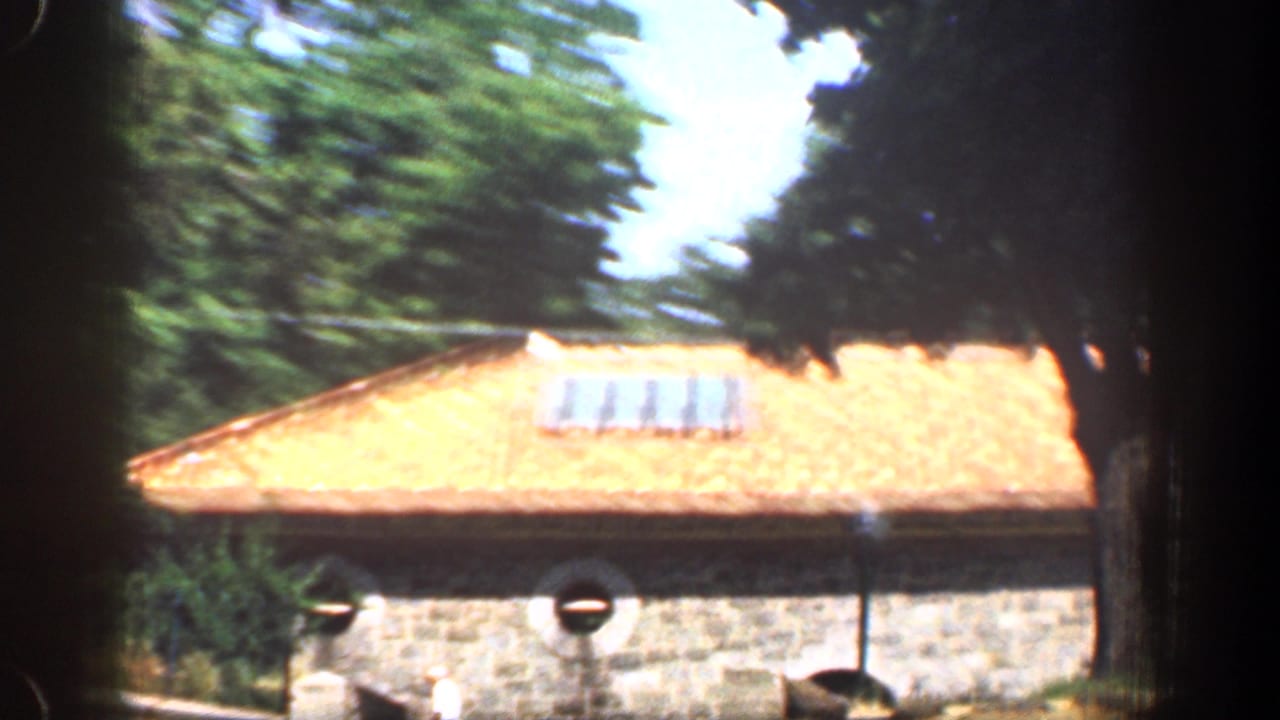 1961 Washington, DC home-movie frame showing a stone building, terracotta roof, and rooftop panel array partly framed by trees.