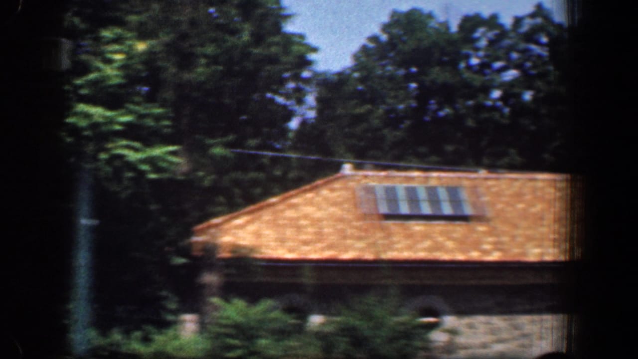 1961 Washington, DC frame showing the same stone building with terracotta roof, rooftop panels, shrubs, and tall trees.