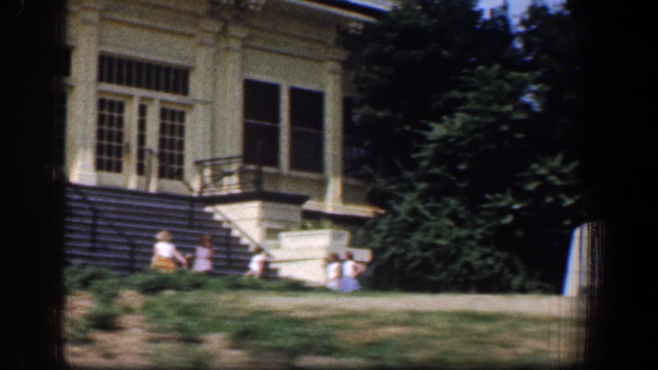 Washington-area 1961 home-movie frame of a light-colored building exterior with steps, windows, railing, trees, and lawn.