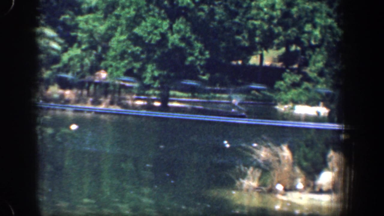 Washington, DC-area 1961 8mm frame with pond water in the foreground, reeds at right, trees, and fence rails behind.