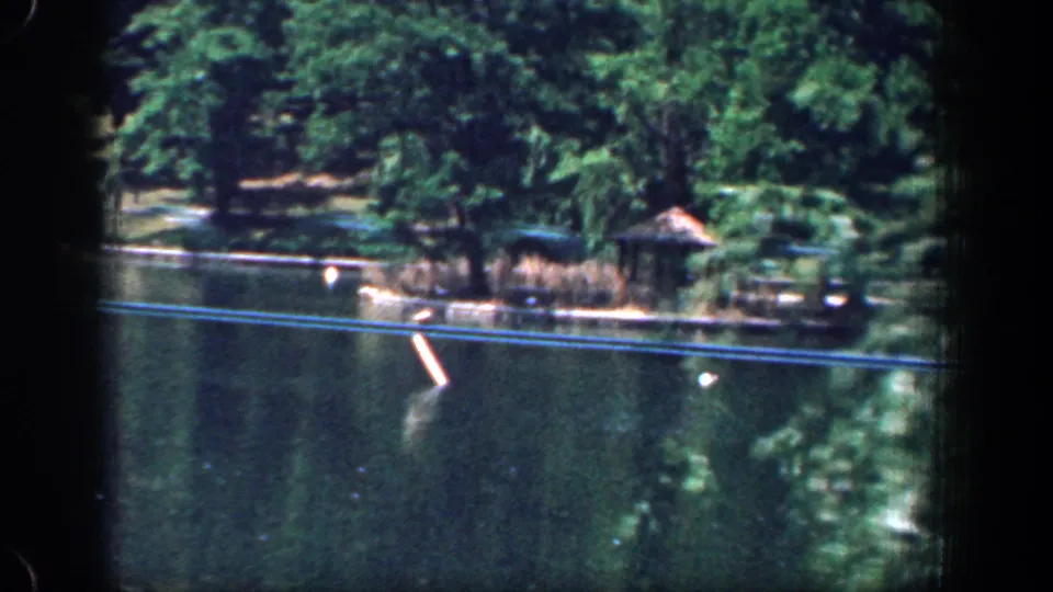 1961 Washington, DC home-movie view of a park lake bordered by trees and shoreline plantings, seen through dark 8mm frame edges.