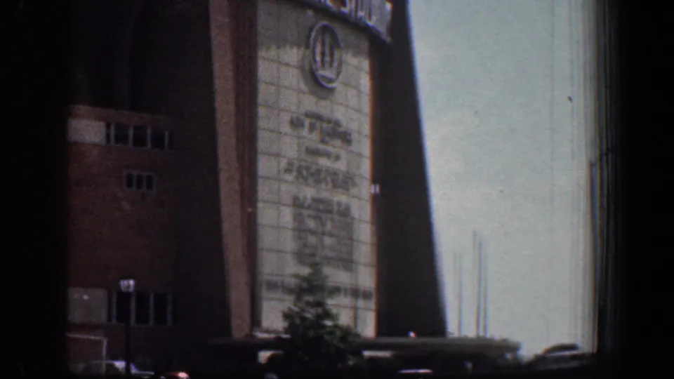 1961 Washington, DC home-movie frame showing Memorial Stadium entrance signage, brick walls, a small tree, and parked cars below.