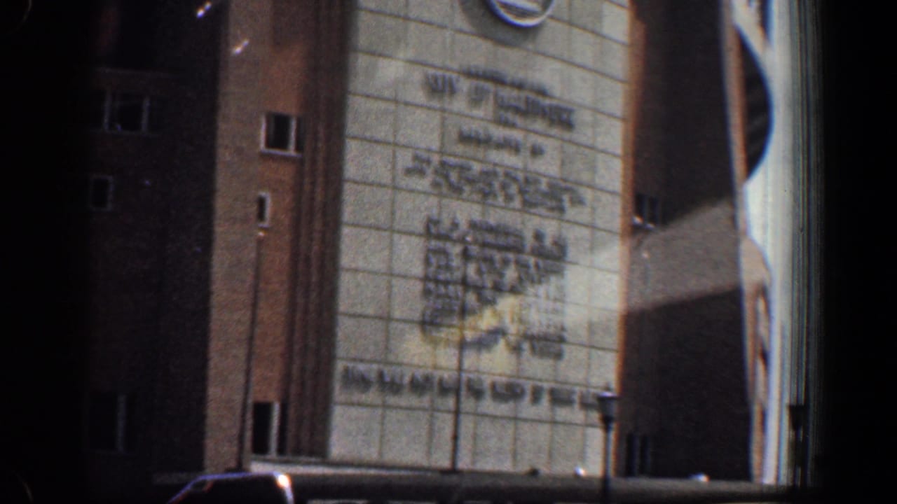 Close 1961 8mm frame of Memorial Stadium entrance in Washington, DC, showing signage, brickwork, windows, and cars near the base.