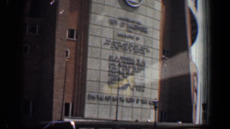 Close 1961 8mm frame of Memorial Stadium entrance in Washington, DC, showing signage, brickwork, windows, and cars near the base.