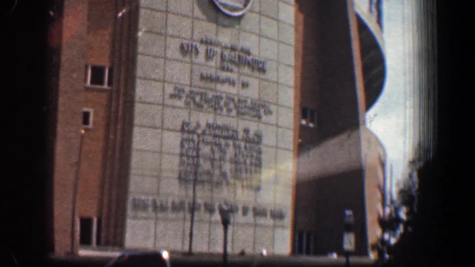 1961 Washington, DC home-movie frame showing a tall modern building facade with inscription, brick sides, curved architecture, and street trees.