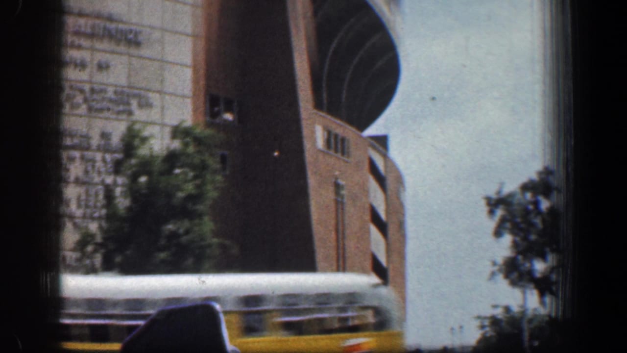 1961 Washington, DC street view with a yellow bus passing below a modern brick-and-panel building with curved architecture.