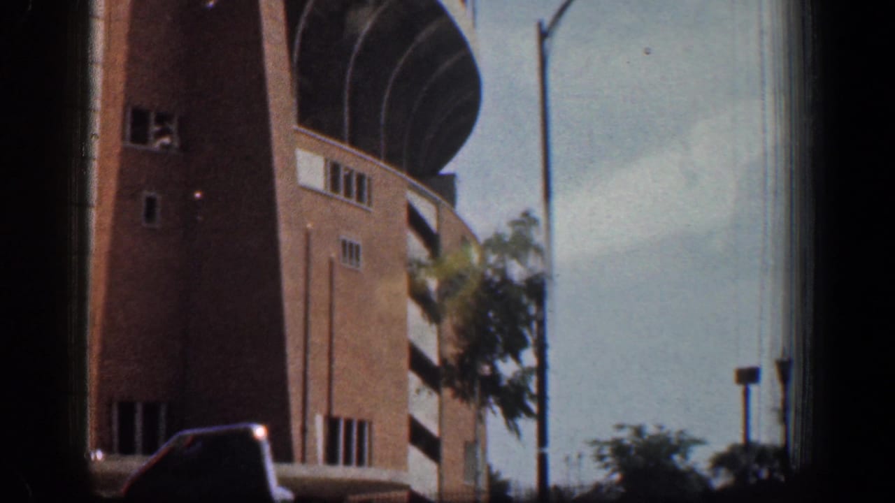 1961 Washington, DC home-movie frame showing a brick tower section, curved upper architectural bands, trees, streetlight, and sky.