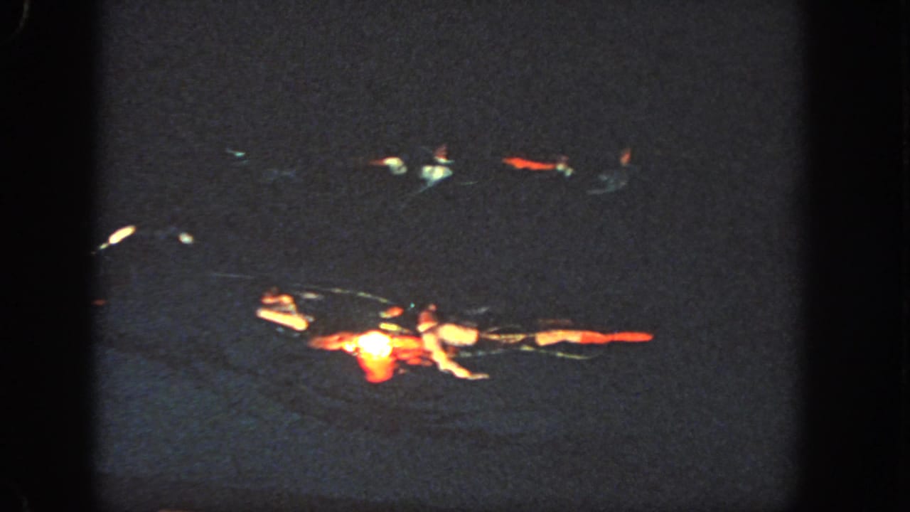 In 1951 Georgia home-movie footage, paired swimmers appear in a dark pool under spotlights, with red and white costume areas catching the light.