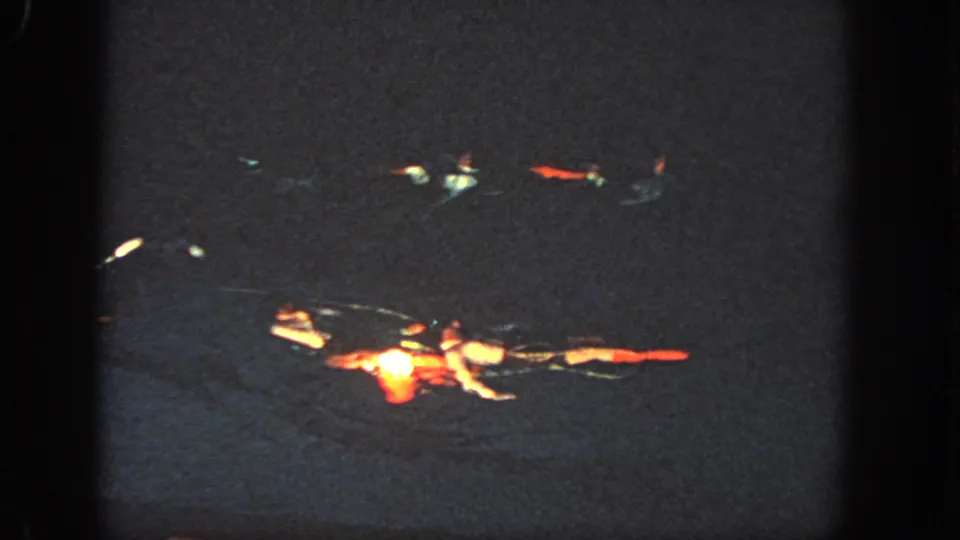 In 1951 Georgia home-movie footage, paired swimmers appear in a dark pool under spotlights, with red and white costume areas catching the light.