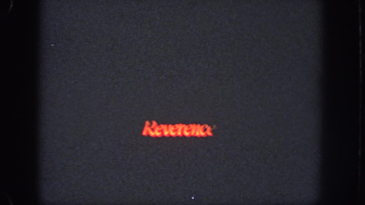 Red "Reverence" lettering on a dark frame above a dim stage scene.