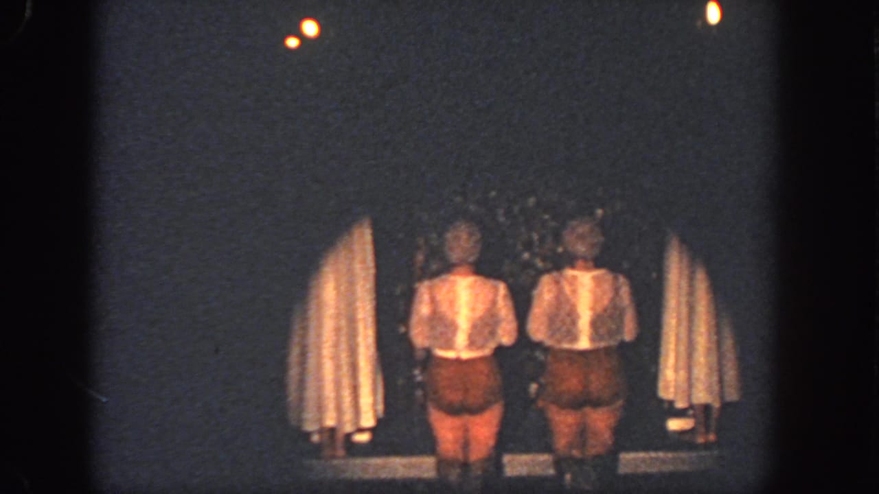 Two costumed performers stand between curtains on a dim Georgia stage in 1951 home-movie footage.