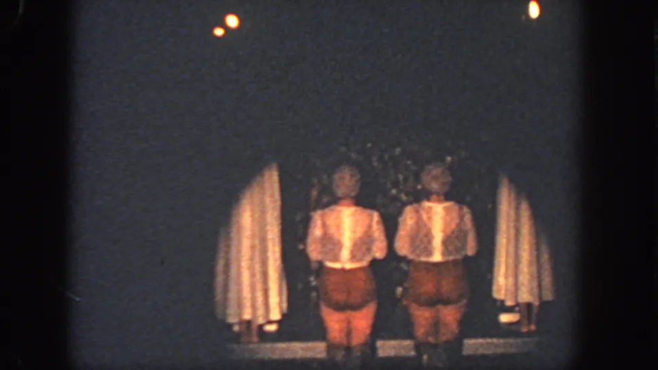 Two costumed performers stand between curtains on a dim Georgia stage in 1951 home-movie footage.