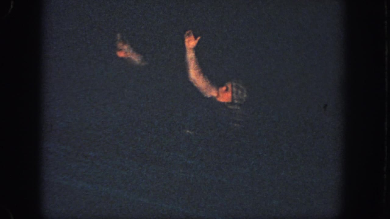 Two swim-capped women in dark pool water with one arm raised.