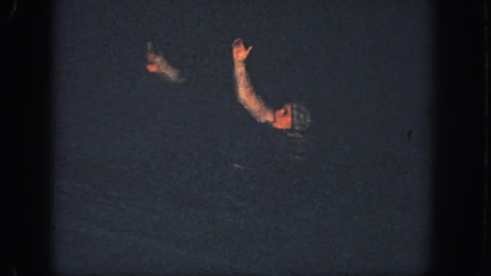 In 1951 Georgia 8mm footage, two women in swim caps appear partly submerged in a dark pool while one raises an arm.