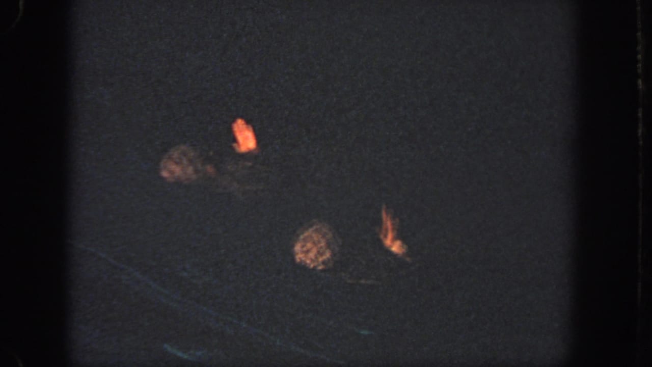 The swimmers cluster closer together in the dark pool, with caps and hands visible as the synchronized movement continues.
