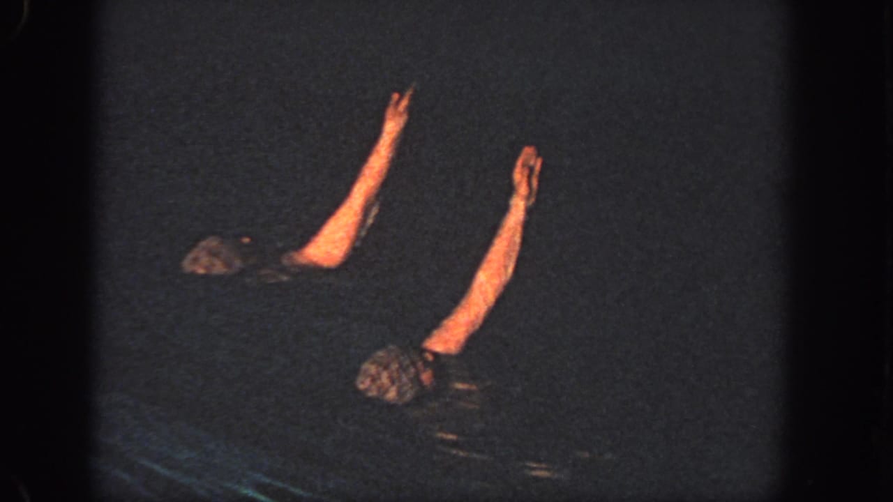 Two swimmers in a dark Georgia pool raise their arms in a synchronized pose in 1951 home-movie footage.
