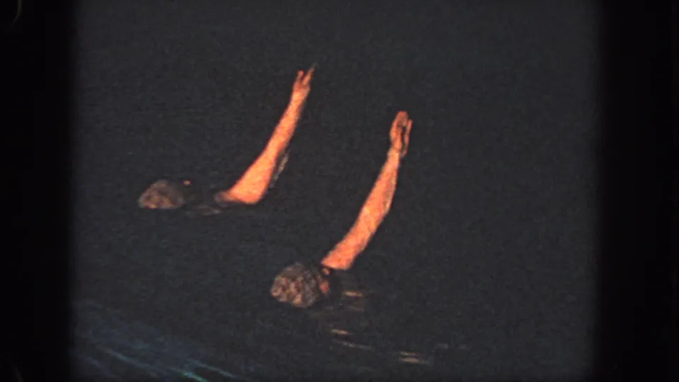 Two swimmers in a dark Georgia pool raise their arms in a synchronized pose in 1951 home-movie footage.