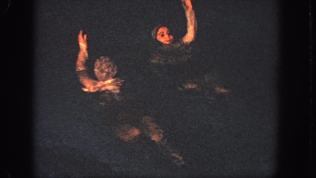 Two swimmers face one another in a dark pool, each raising an arm during the Georgia 1951 synchronized sequence.