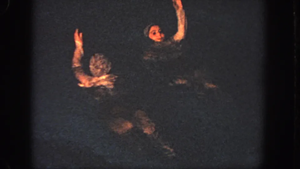 Two swimmers face one another in a dark pool, each raising an arm during the Georgia 1951 synchronized sequence.