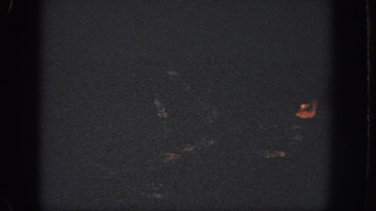 A dim 1951 home-movie frame shows a swimmer mostly obscured by darkness, with a face and faint body shape in the water.