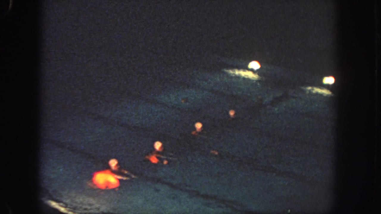 1951 Georgia home-movie frame showing several synchronized swimmers in red costumes crossing a dimly lit pool at night.