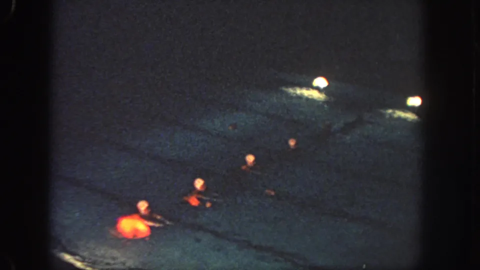 1951 Georgia home-movie frame showing several synchronized swimmers in red costumes crossing a dimly lit pool at night.