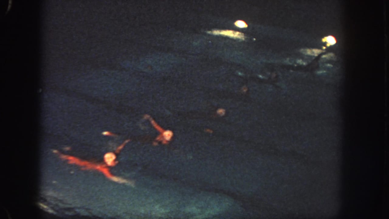 1951 Georgia footage frame with synchronized swimmers in red costumes extending their arms during a nighttime pool routine.