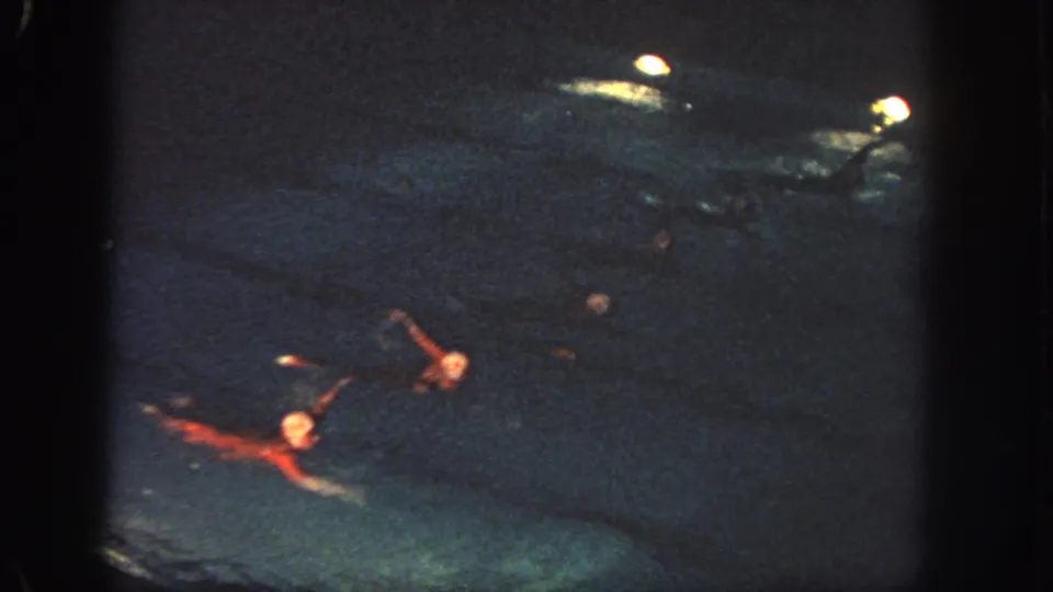 1951 Georgia footage frame with synchronized swimmers in red costumes extending their arms during a nighttime pool routine.