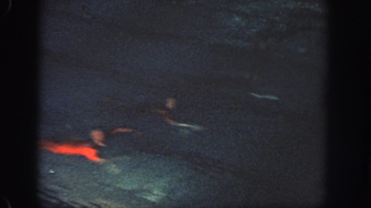 1951 Georgia home-movie frame showing a red-costumed swimmer moving through dim pool water with other figures faintly visible.