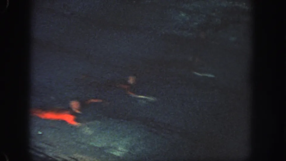 1951 Georgia home-movie frame showing a red-costumed swimmer moving through dim pool water with other figures faintly visible.