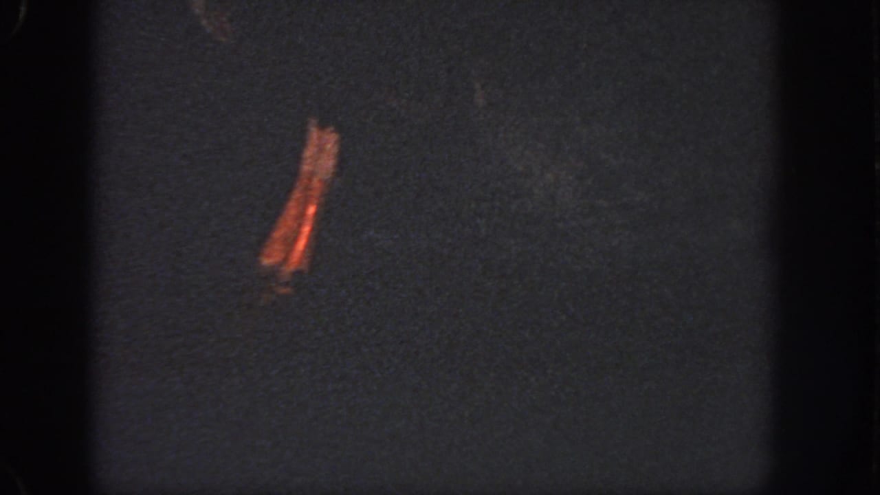 Low-exposure 1951 Georgia 8mm frame with dark water, a prominent orange-brown stain, grain, and edge shadows.
