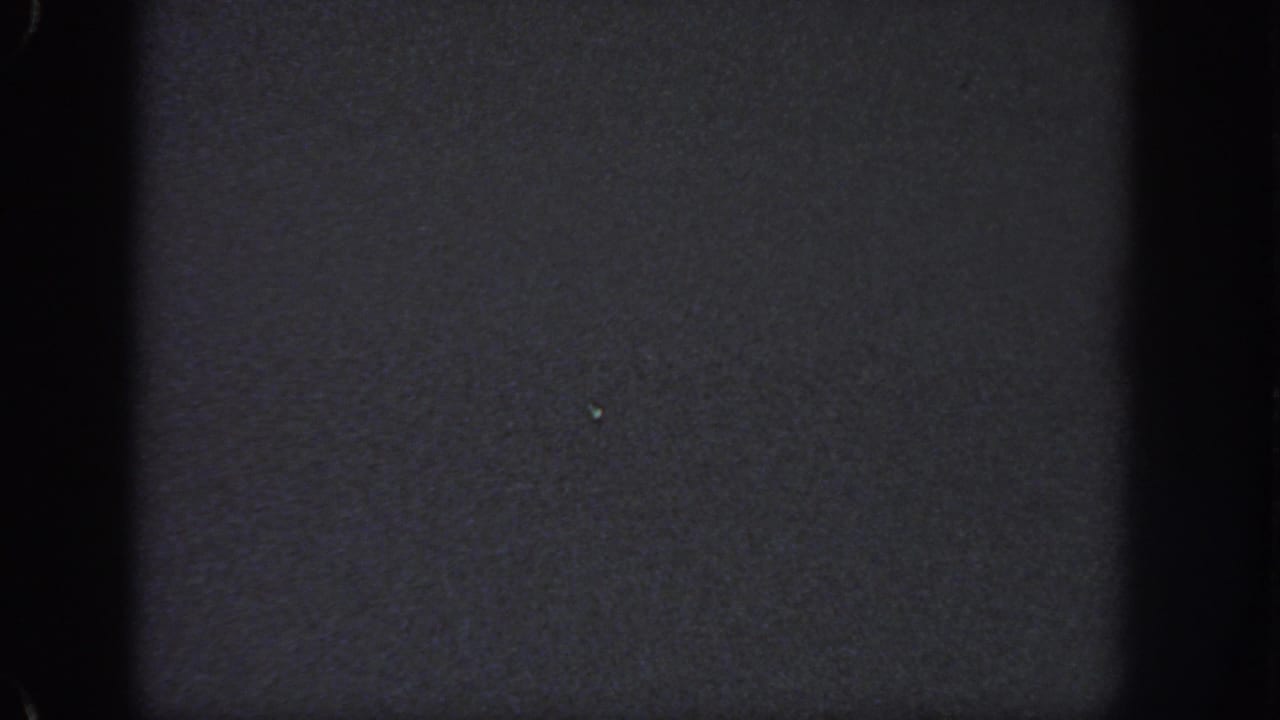 Very dark 8mm frame from the Georgia clip with minimal visible detail, faint specks, and film gate edges.