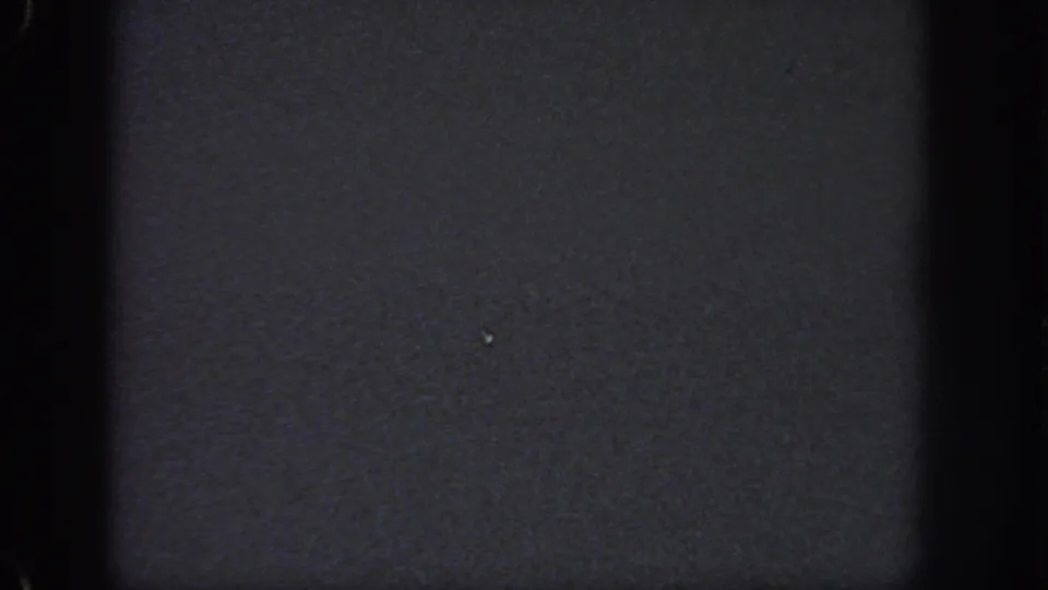 Very dark 8mm frame from the Georgia clip with minimal visible detail, faint specks, and film gate edges.